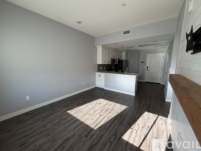 A spacious room with wooden flooring and a kitchen area in the background.