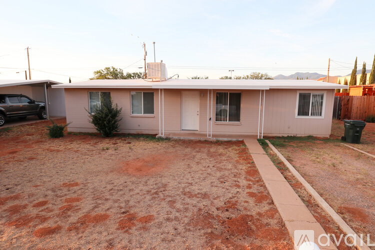A house with a brown dirt yard and a black car parked in the driveway.