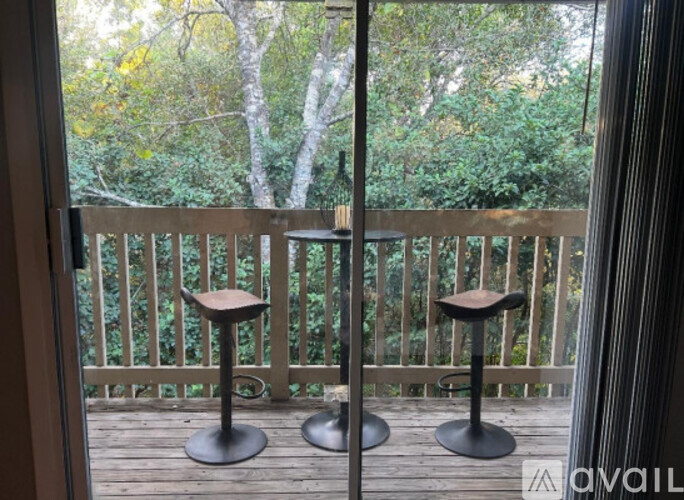 Two stools are on a wooden deck with a view of trees.