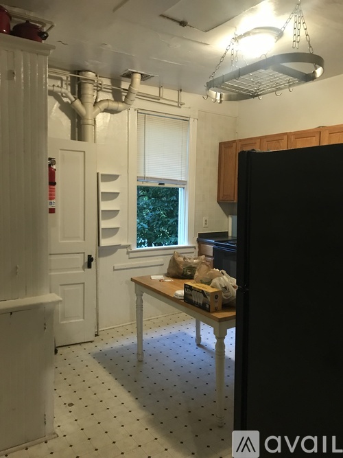 A kitchen with a black fridge, white walls and a wooden table.