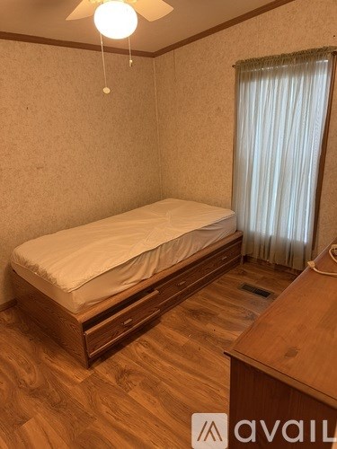 A bedroom with a bed, desk, and window with curtains.