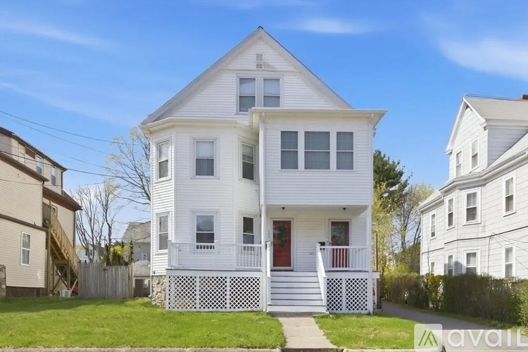 A two-story white house with a red door and a white picket fence.