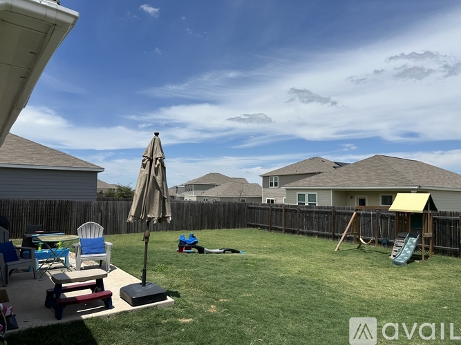 A backyard with a patio table and chairs, an umbrella, and a swing set.