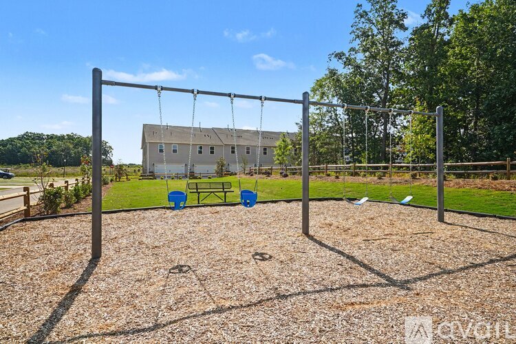 A playground with swings and a seesaw in the foreground and a building in the background.