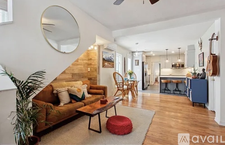 A living room with a brown couch, a round mirror, and a wooden staircase.