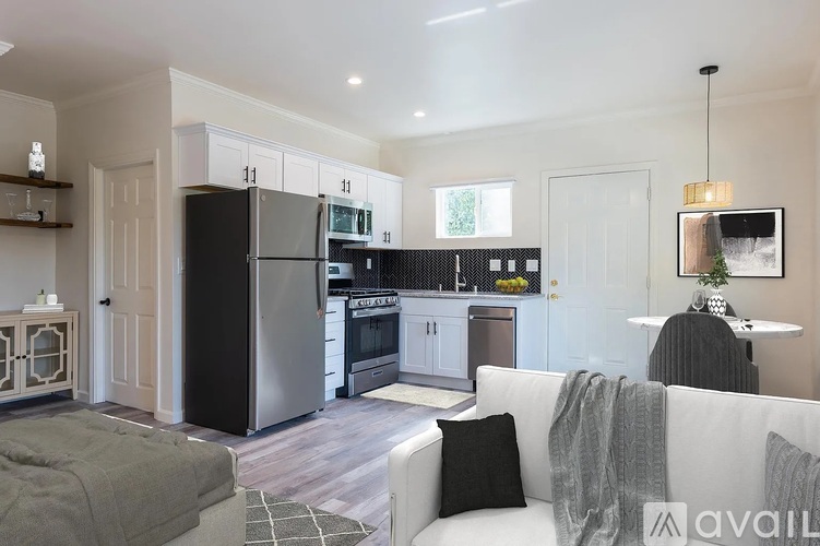 A modern kitchen with a black fridge and stove, a dining table with chairs, and a living area with a sofa and a coffee table.