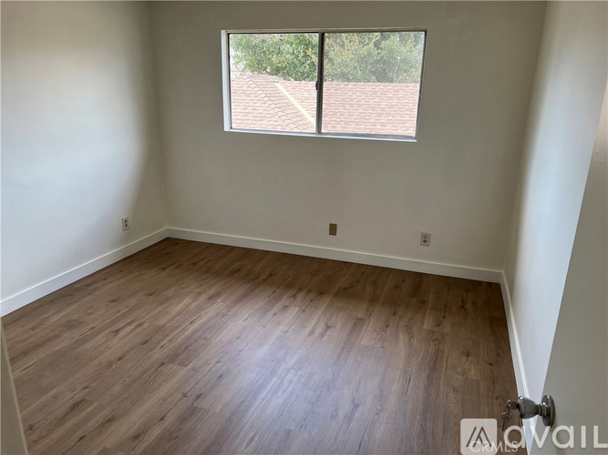 A room with wooden flooring and a window overlooking a roof.
