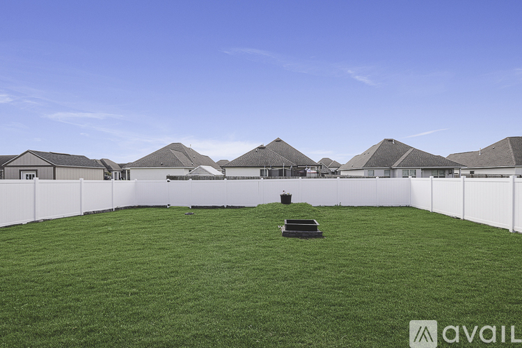A grassy field with a white fence and houses in the background.