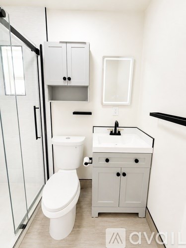 A white toilet sits in a bathroom next to a sink and medicine cabinet.