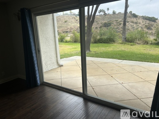 A room with a sliding glass door leading to a patio with a view of a green hill.