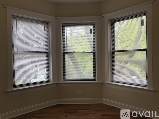 Three windows with blinds open to a view of trees and a house.