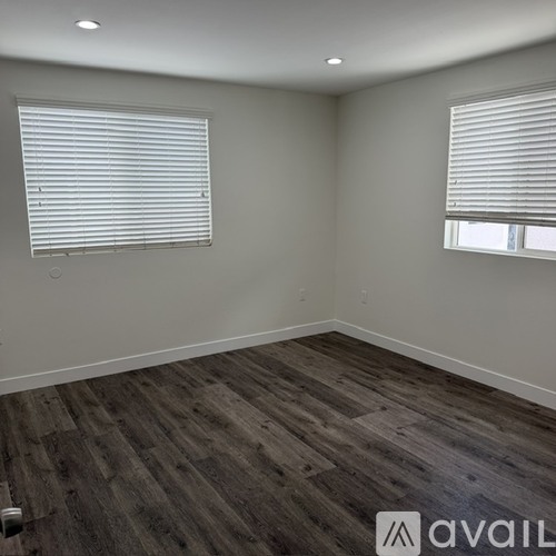 A room with wooden flooring and two windows with blinds.
