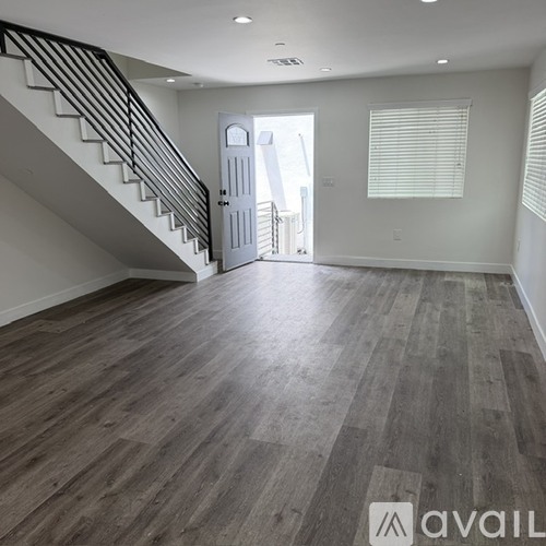 A spacious room with wooden flooring and a staircase leading to another level.