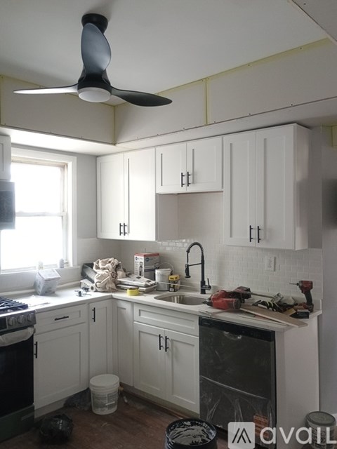 A kitchen with white cabinets and a black fan.