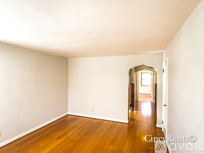 A room with wooden floors and white walls, with a doorway leading to another room.