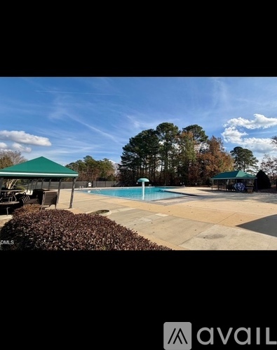 A pool surrounded by a green roofed pavilion and trees.