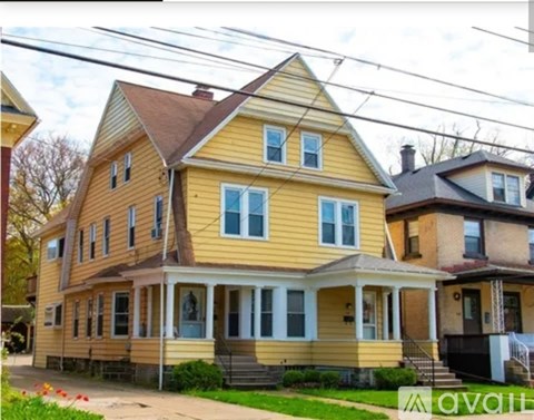 A yellow house with a brown roof and a porch.