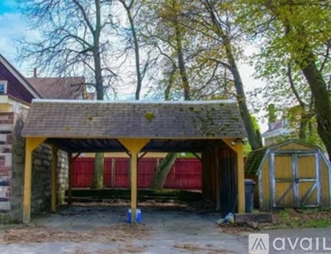 A small wooden structure with a red door is surrounded by trees.