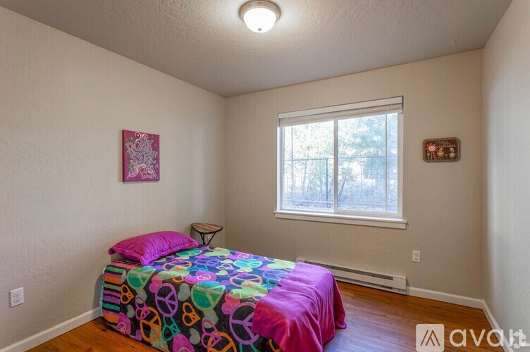 A bedroom with a colorful bedspread and a window.
