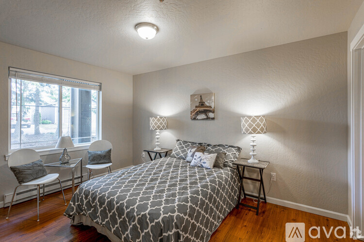 A bedroom with a bed, two chairs, and a table with a lamp on it.
