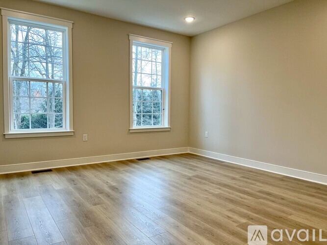 A room with wooden flooring and two windows.
