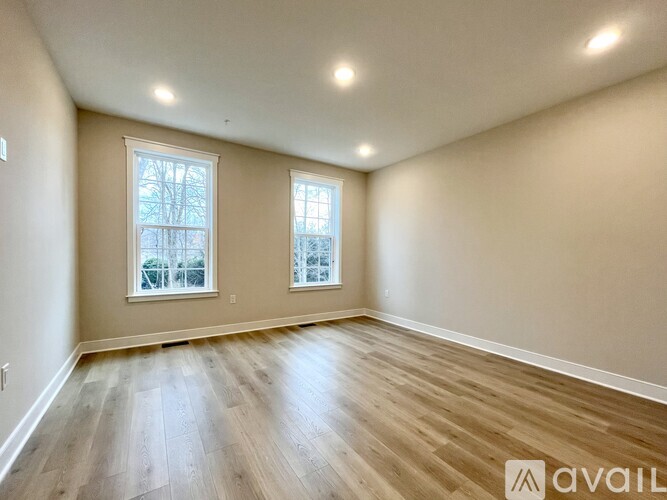 A spacious room with wooden flooring and two windows.