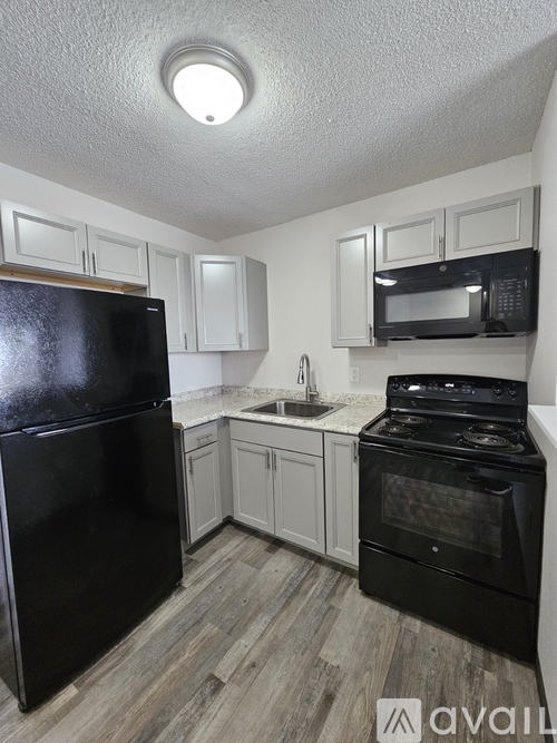 A black refrigerator is in a kitchen with white cabinets and a black stove.