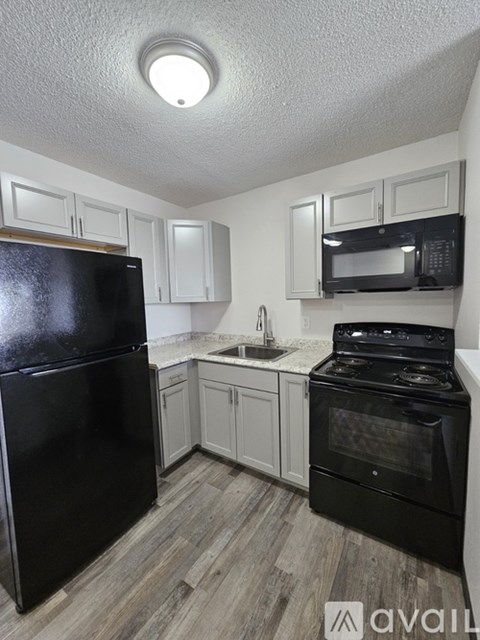 A black refrigerator is in a kitchen with white cabinets and a black stove.