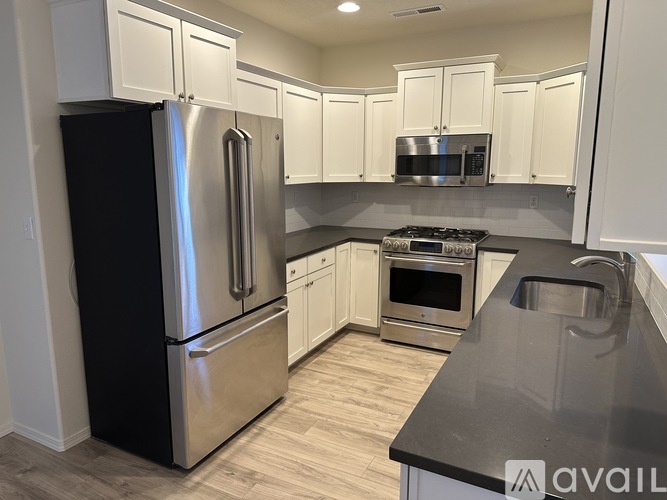 A kitchen with a black refrigerator, stainless steel appliances, and white cabinets.