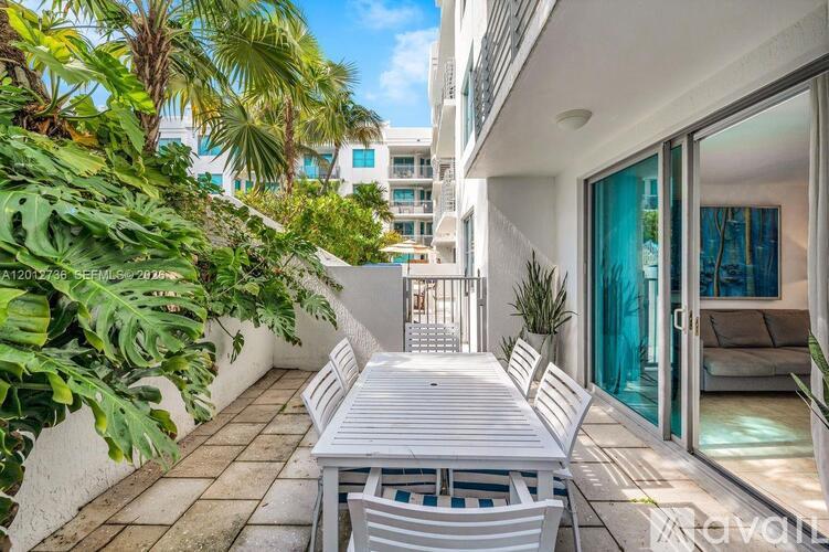 A white table and chairs are on a patio with a glass door and a plant.