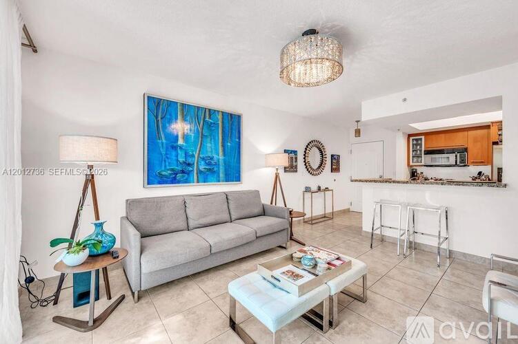 A living room with a grey couch, a wooden table with a plant and a vase on it, a white chair, a white sofa, a white coffee table, a white fridge, a white microwave, a white o