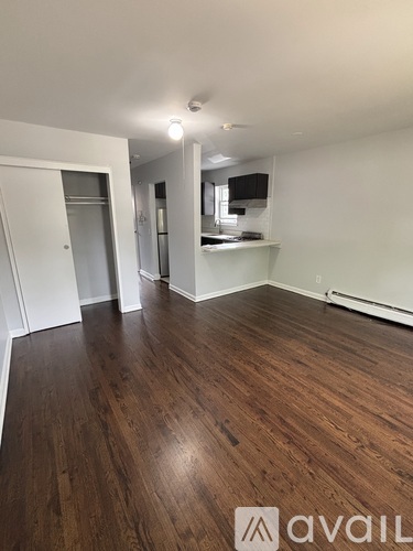 A room with wooden floors and a kitchen area in the background.