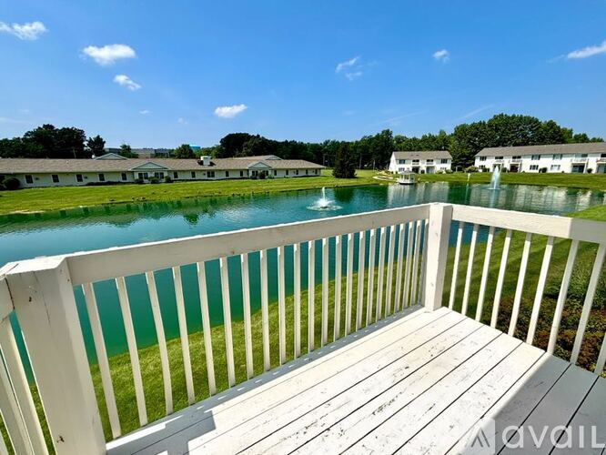 A white deck overlooks a green pond and a white building.