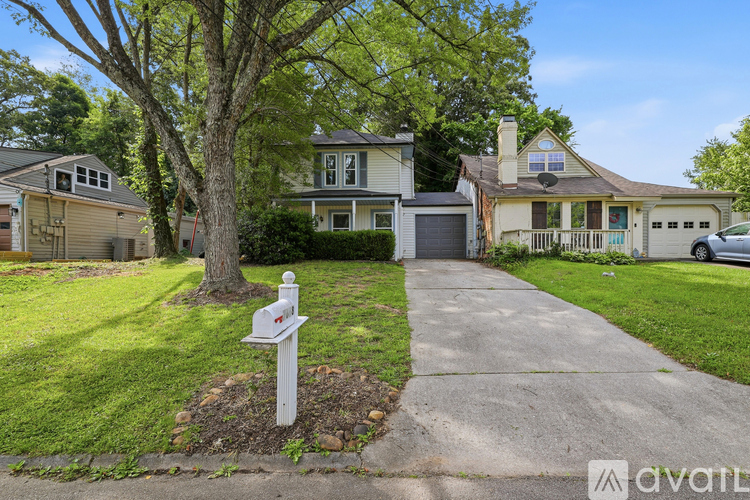 A tree stands in front of a house with a mailbox on the sidewalk.