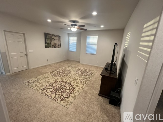 A living room with a rug, a ceiling fan, and a painting on the wall.