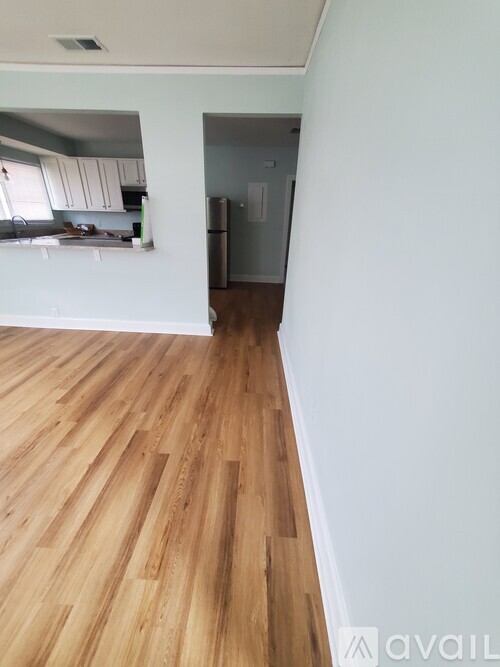 A room with wooden flooring and a kitchen area in the background.