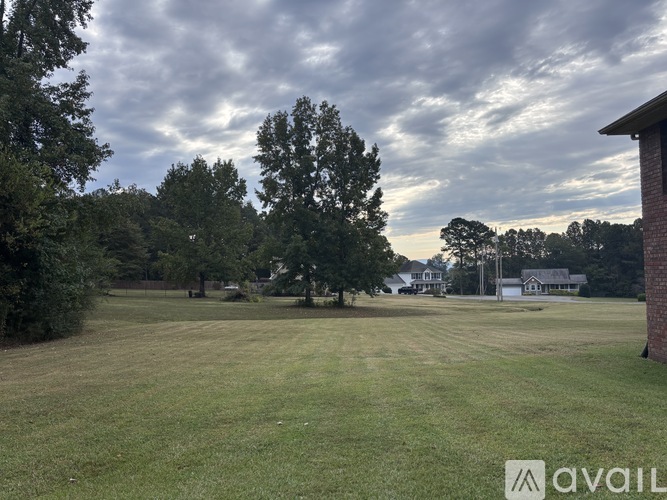 A grassy field with trees and houses in the background.