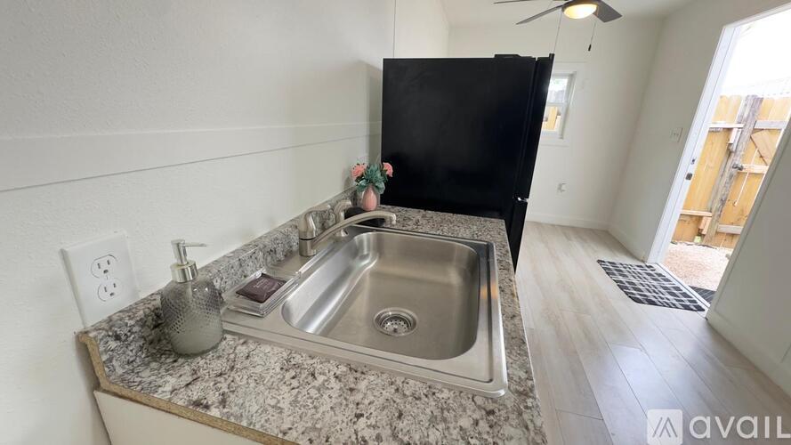 A kitchen sink with granite countertop and a black refrigerator in the background.