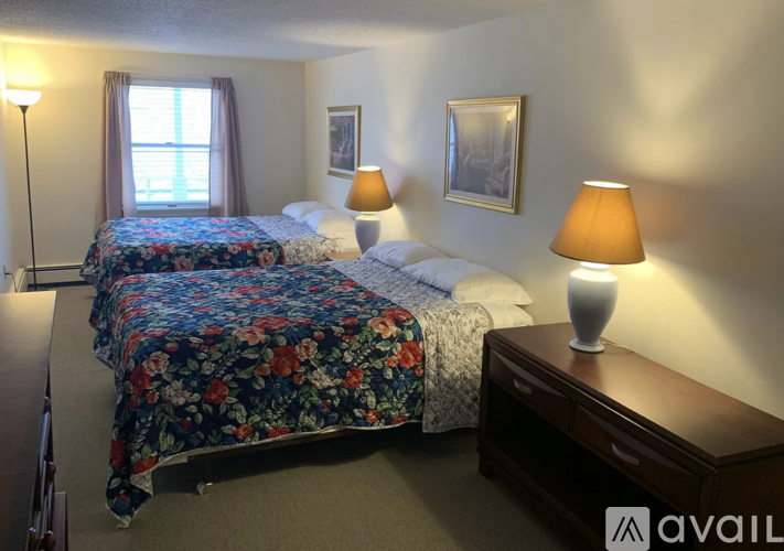 A bedroom with two beds and a nightstand with a lamp.
