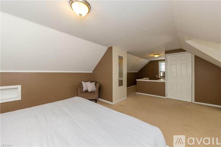 A bedroom with a white bed and a brown chair.