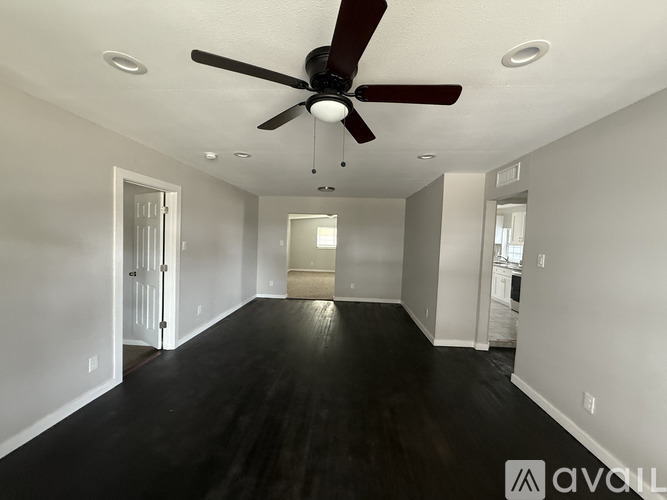 A spacious room with a ceiling fan and dark hardwood floors.