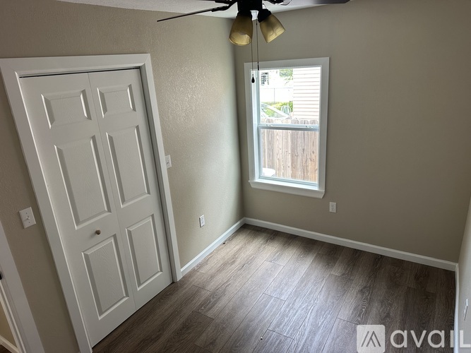 A room with a white door and a window with a view of a fence and trees outside.