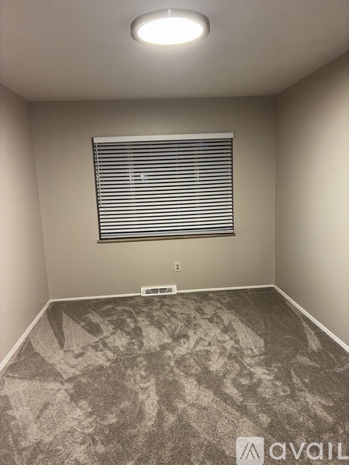 A room with a carpeted floor and a window with blinds.