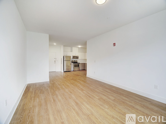 A room with wooden flooring and white walls, with a small kitchenette in the corner.