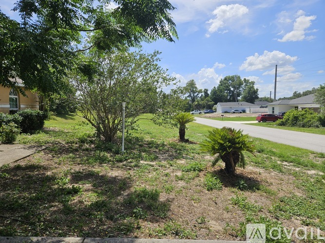 A sunny day in a residential area with a house, trees, and a street visible.