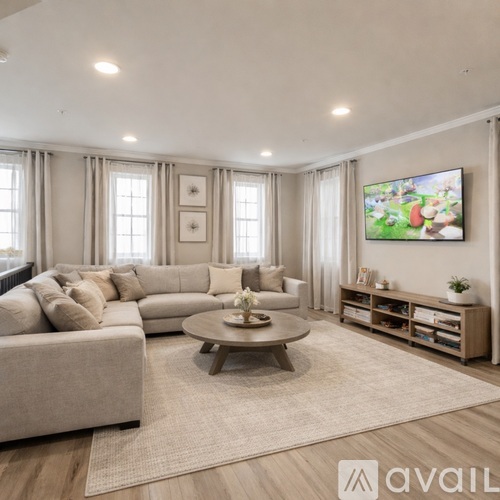 A living room with a large couch, a coffee table, and a flat-screen TV mounted on the wall.