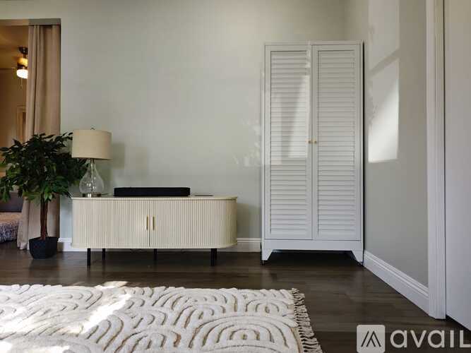 A white room with a rug, a cabinet, and a plant.
