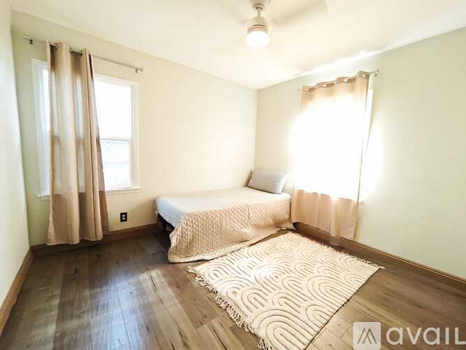 A bedroom with a bed, a window with curtains, and a rug on the floor.
