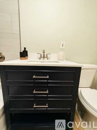 A black bathroom vanity with a white sink and a toilet in the background.