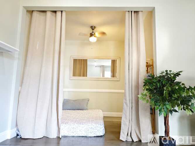 A bedroom with a bed, a mirror, a plant, and a ceiling fan.